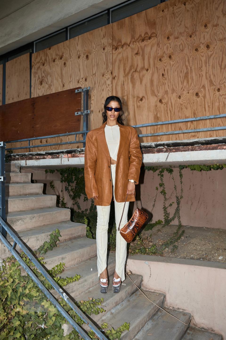 Miro wears a Sami Miro Vintage asymmetric tee and pants in ivory mesh with a vintage leather blazer, Manu Atelier purse, and Veneda Carter x Flatist Eyewear Sunnies.