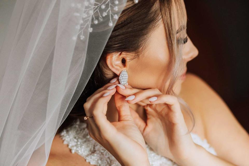 <p>Docinets Vasil/Getty</p> A bride fastens an earring.