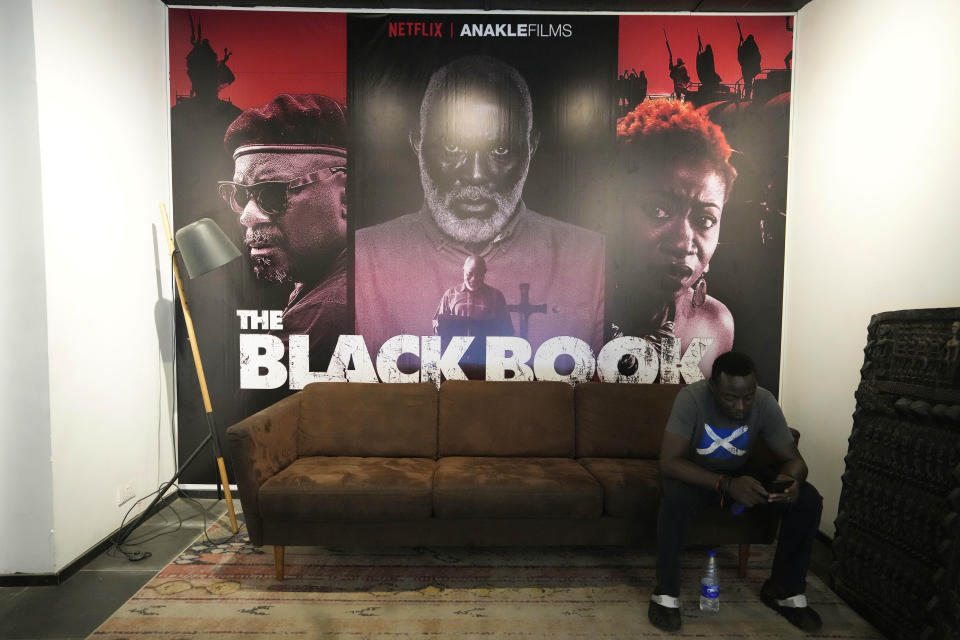 A man reads messages on his mobile phone under a poster of the film The Black Book in Lagos Nigeria. Friday, Oct. 20, 2023. A Nigerian action thriller that tells the gripping story of corruption and police brutality in Africa’s most populous country has reached record viewership numbers on Netflix charts globally. It's a reminder of the power and potential of Nigeria's rapidly growing film industry. (AP Photo/Sunday Alamba)