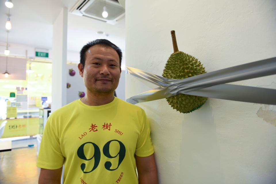 This photo taken on December 12, 2019 shows Singaporean Kelvin Tan, the co-owner of 99 Old Trees, a durian shop in Singapore, posing with his parody of the 120,000 USD artwork Comedian by Maurizio Cattelan. - Inspired by a 120,000 USD artwork, a banana taped to a wall, Tan put his own spin on the piece, captioning it "looks like art, smells like fart" in a widely-shared post. (Photo by CATHERINE LAI/AFP via Getty Images)