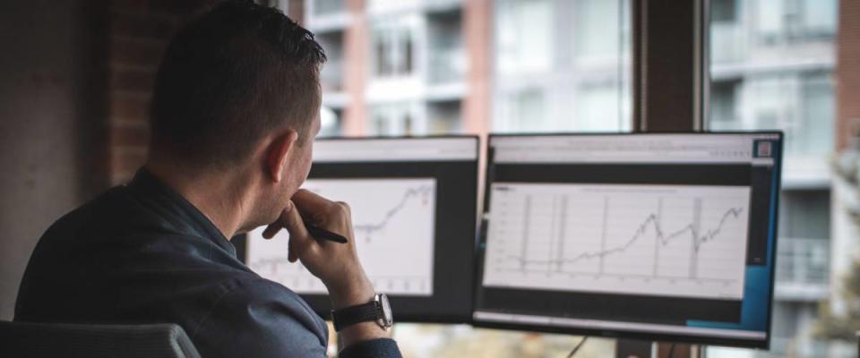 Man looks at computer screen with charts on it, hand to his chin.