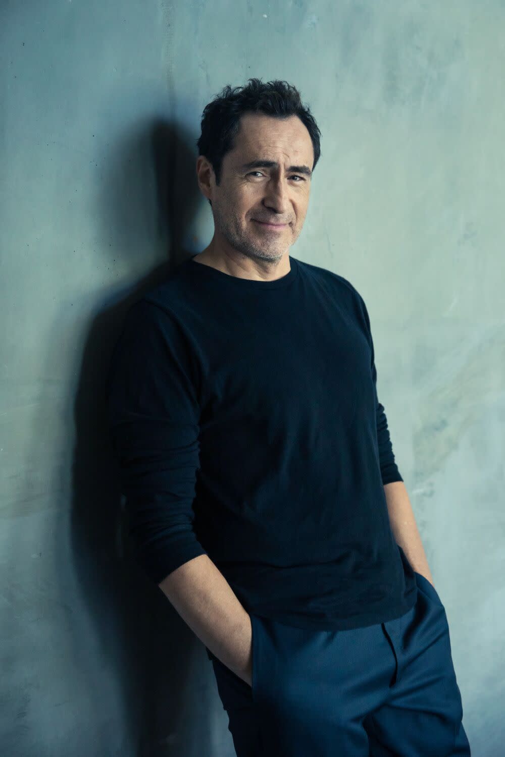 Actor Demian Bichir leans against a blue wall.