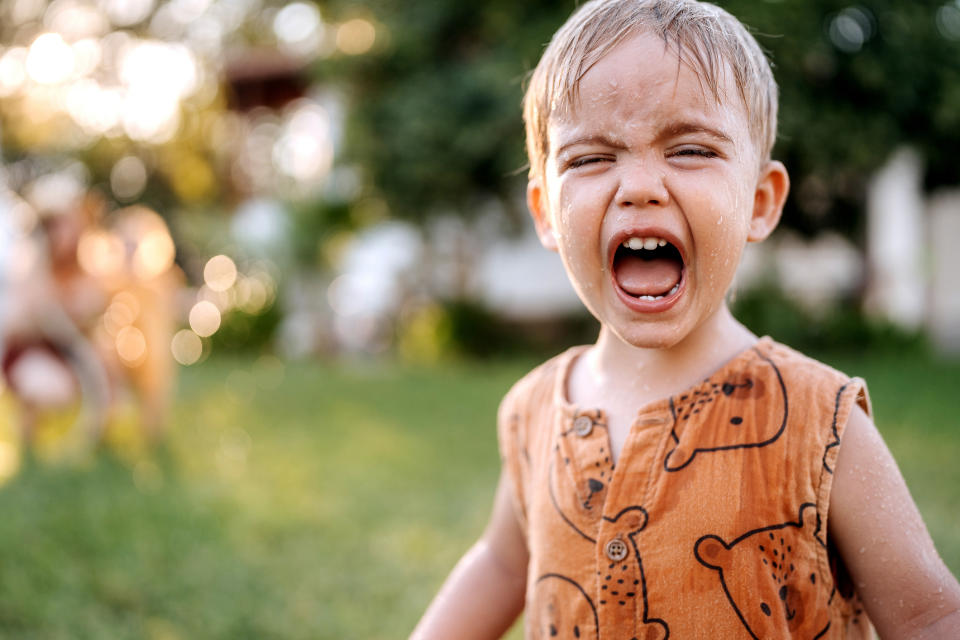 A young child is outdoors, wearing a sleeveless shirt with bear prints, and appears to be crying or shouting