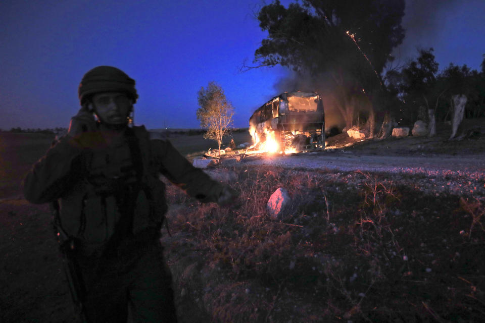 An Israeli soldier stands near a burning bus after it was hit by a mortar shell fired from Gaza near the Israel Gaza border, Monday, Nov. 12, 2018. (AP Photo/Tsafrir Abayov)