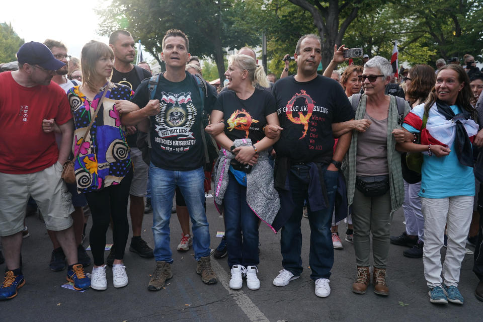 BERLIN, GERMANY - AUGUST 29: A man wearing a right-wing t-shirt and a couple wearing QAnon shirts face off against riot police on Unter den Linden avenue during protests against coronavirus-related restrictions and government policy on August 29, 2020 in Berlin, Germany. Tens of thousands of people from a wide spectrum, including coronavirus skeptics, conspiracy enthusiasts, hippies, right-wing extremists, religious conservatives and others converged on Berlin to attend the protests. City authorities had banned the protests, citing the flouting of social distancing by participants in a similar march that drew at least 17,000 people a few weeks ago, but a court overturned the ban. / Credit: / Getty Images