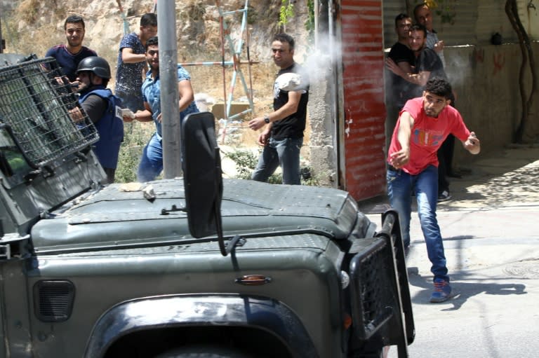 A Palestinian throws a stone towards a vehicle of Israeli security forces during clashes on July 31, 2015 in the West Bank town of Hebron