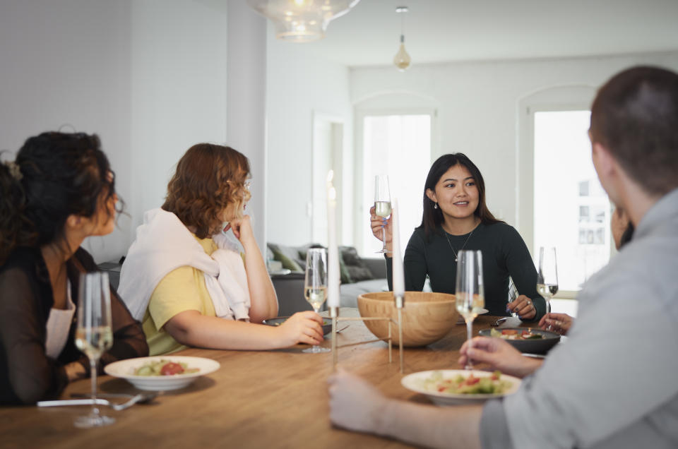 Group of young people enjoying dinner party at home. Multiracial group of male and female friends sitting at table having drinks at talking.