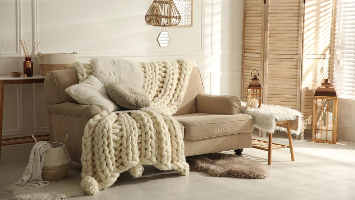 cozy living room interior with beige sofa, knitted blanket and cushions
