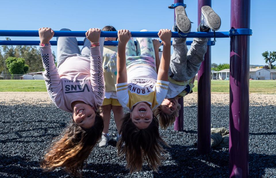 Irma Segura, left, hangs upside down with her sister Paloma Segura, middle and a classmate during recess inside San Antonio Elementary School in Lockwood, Calif., on Wednesday, May 11, 2022. Irma, currently a 3rd grader, is in the same class as her sister Paloma in 3rd grade. 
