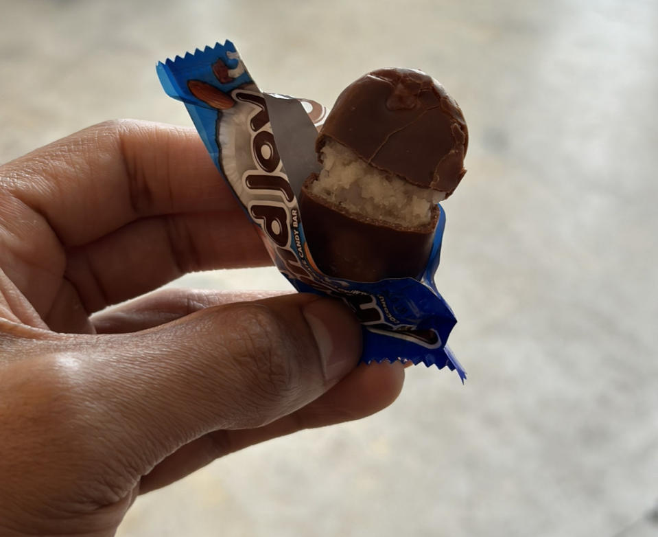 A hand holding an Almond Joy chocolate bar, showing the coconut inside, in an open bag