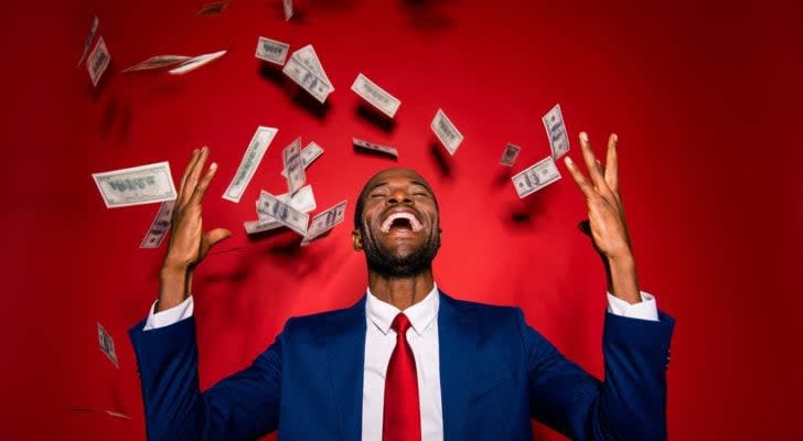 Man in blue formal wear tuxedo standing as money 'rains' on him, isolated on red vivid background.