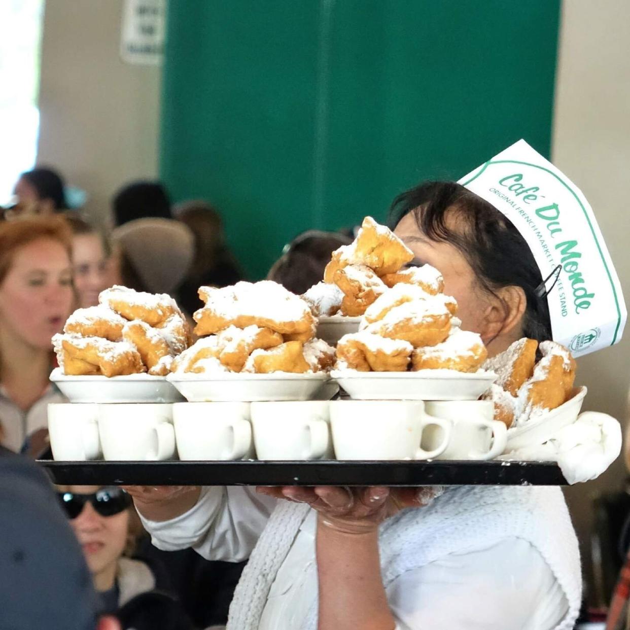 A server at New Orleans' legendary Cafe Du Monde carries a tray of coffee and fresh beignets. (Photo: Visit New Orleans)