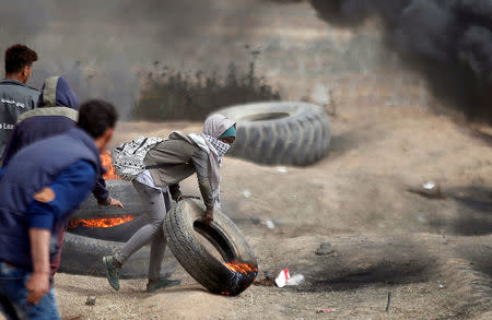 Female demonstrator Aya moves a burning tire during a protest where Palestinians demand the right to return to their homeland, at the Israel-Gaza border, east of Gaza City April 20, 2018. REUTERS/Mohammed Salem