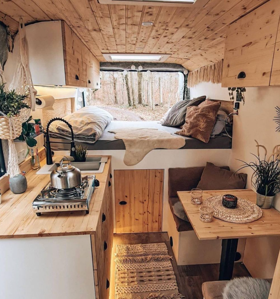 <span class="caption">Interior of a custom converted van including wood benchtops, seating area, and bed with styled bedding.</span> <span class="attribution"><span class="source">@sprintercaravans/Instagram</span></span>