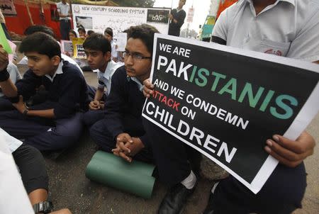 Students sit and hold placards for the victims of the Taliban attack on the Army Public School in Peshawar, along a road in Karachi December 19, 2014. REUTERS/Akhtar Soomro