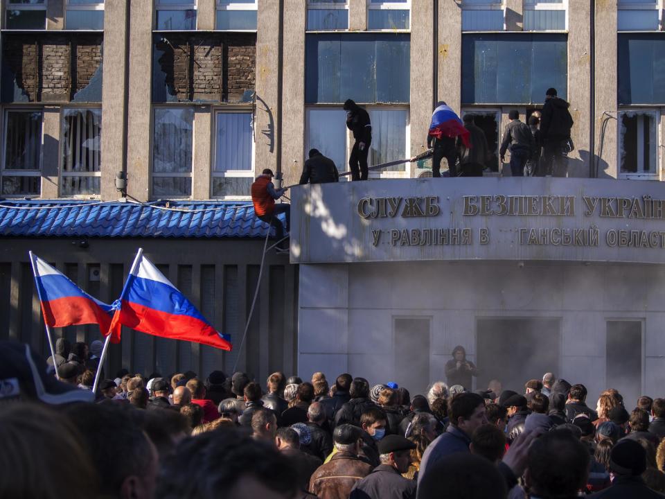 Pro-Russian activists with Russian national flags storm the Ukrainian regional office of the Security Service in Luhansk, Ukraine, Sunday, April 6, 2014. In Luhansk, 30 kilometers (20 miles) west of the Russian border, hundreds of people surrounded the local headquarters of the security service and later scaled the facade to plant a Russian flag on the roof. (AP Photo/Igor Golovniov)