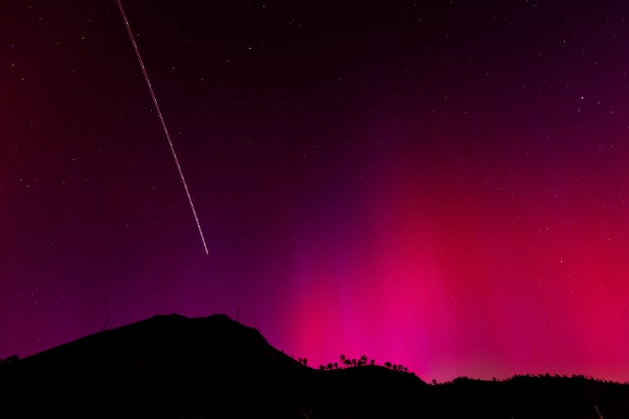 The blinking lights of a plane streak through the Aurora Borealis, also known as the Northern Lights, which is visible over Lake Berryessa, Calif., early Saturday, May 11, 2024. (Carlos Avila Gonzalez/San Francisco Chronicle via AP)