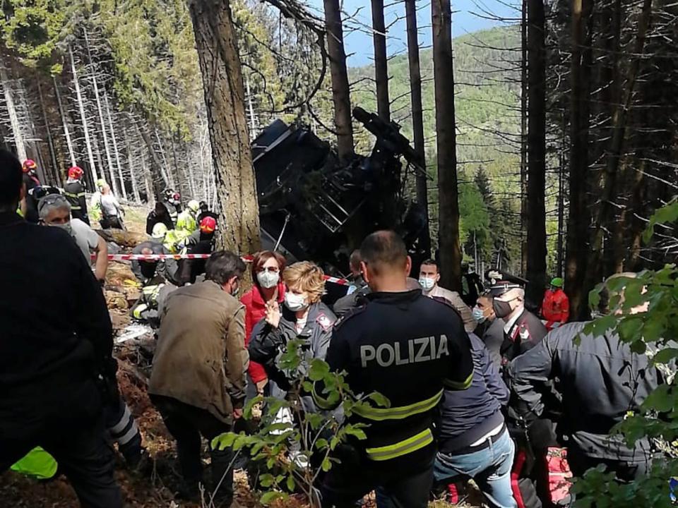 A view of the crashed cable car with numerous people and Lake Maggiore in the background.