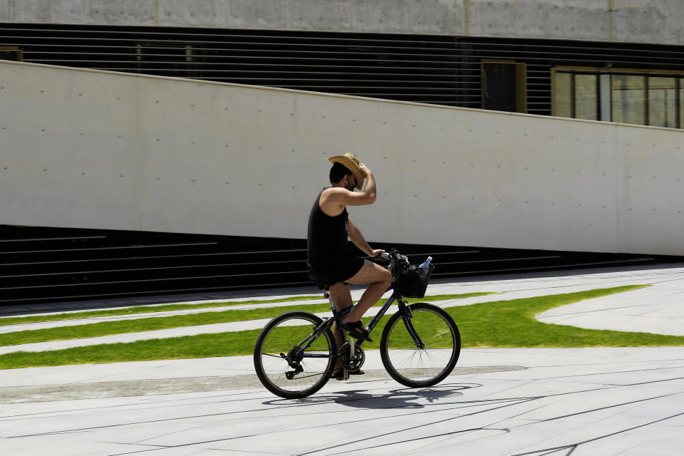 A man adjusts his hat as he's drives his bicycle amid hot weather at Eleftherias, Liberty, square in central capital Nicosia, Cyprus, on Friday, June 14, 2024. (AP Photo/Petros Karadjias)