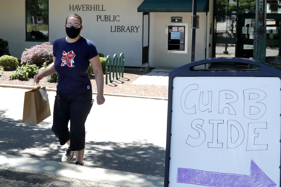 Librarian Emily Giguere delivers books to a reader waiting in his car outside the Haverhill Library, Wednesday, June 17, 2020, in Haverhill, Mass. Libraries are closed for interior use due to coronavirus concerns. (AP Photo/Elise Amendola)