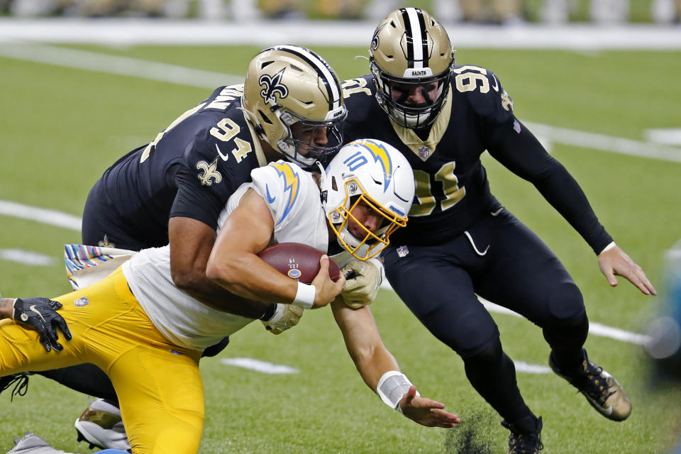 Los Angeles Chargers quarterback Justin Herbert (10) carries as he is tackled by New Orleans Saints defensive end Cameron Jordan (94) and defensive end Trey Hendrickson (91) in the first half of an NFL football game in New Orleans, Monday, Oct. 12, 2020. (AP Photo/Brett Duke)