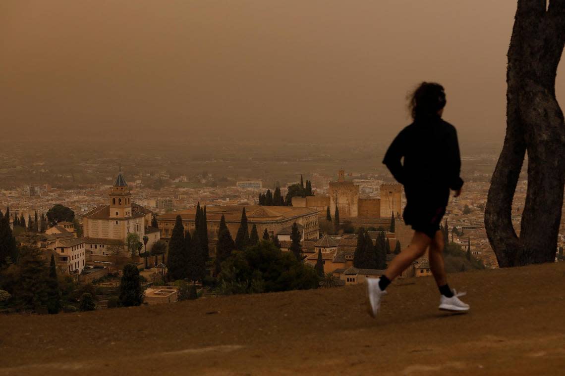 A man runs with a view of the Alhambra monument in Granada while the city is covered by a Saharan dust haze on March 24, 2022.