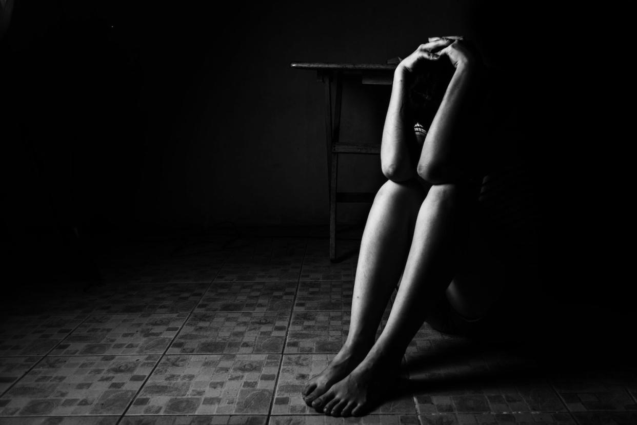 A black and white photo of a person sitting down on the floor with his hands clasped in a praying position