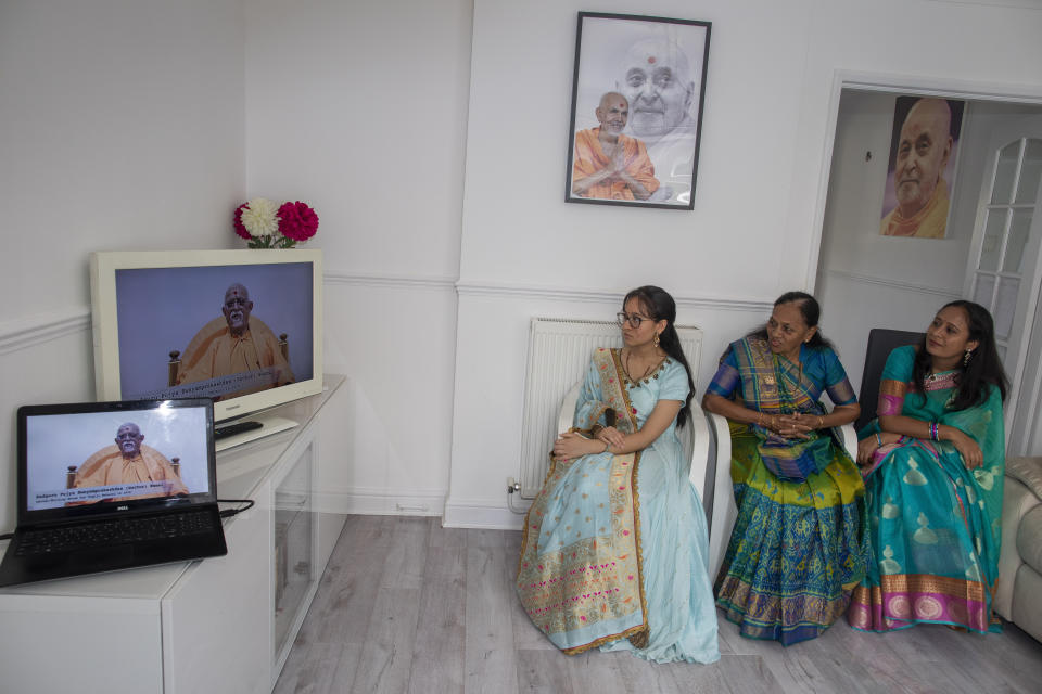 Aagna Patel, de 16 años, Pushpa Patel, de 68, y Hemali Patel, de 42, vestidas con sus mejores saris, escuchan al guru Pujya Swayamprakashdas en el televisor de su sala en Hemel Hempstead, Inglaterra, 14 de junio de 2020. (AP Foto/Elizabeth Dalziel)