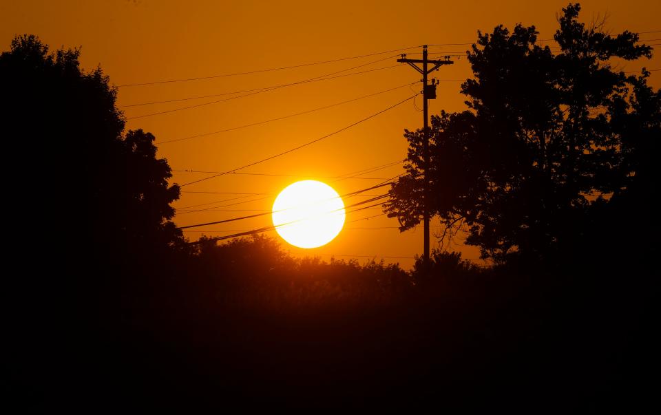The sun casts an orange glow as it sits over Floyd County, Indiana, as utility poles for power lines are silhouettes Tuesday. Temperatures were expected to hit in the high 90s with heat index around 110 degrees. Jackson County REMC issued a statement to its customers in Southern Indiana last Sunday indicating the possibility of "rolling blackouts in the region this summer."