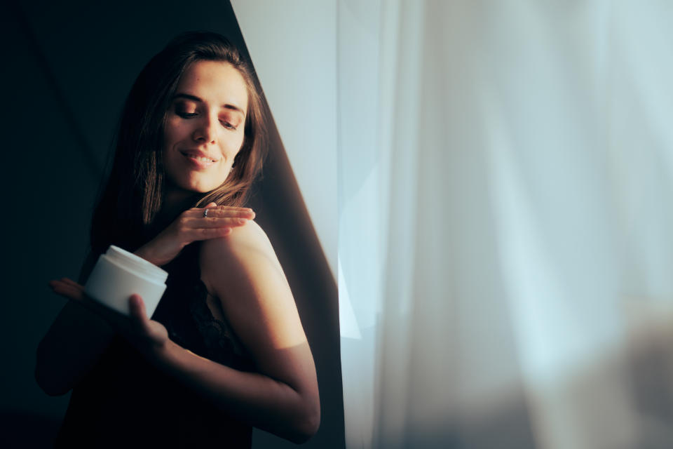 woman applies skin cream to her shoulder. Eczema concept. Image via Getty Commercial.