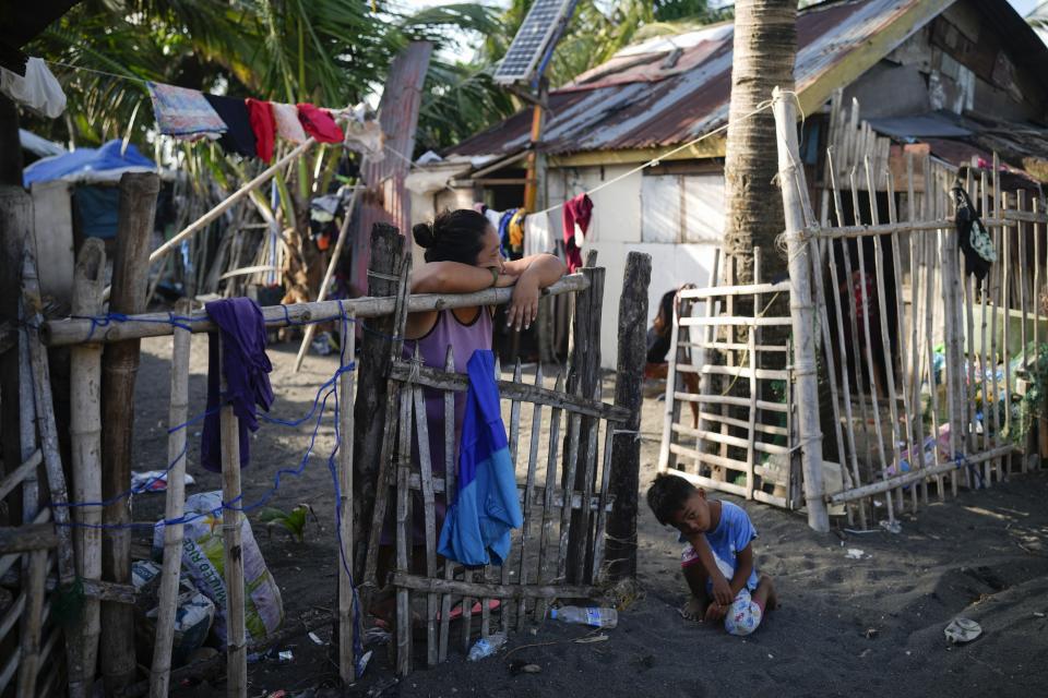 A woman waits outside her house near a liquified natural gas power plant in Santa Clara, Batangas province, Philippines on Tuesday, Aug. 8, 2023. The Philippines is seeing one of the world's biggest buildouts of natural gas infrastructure. (AP Photo/Aaron Favila)