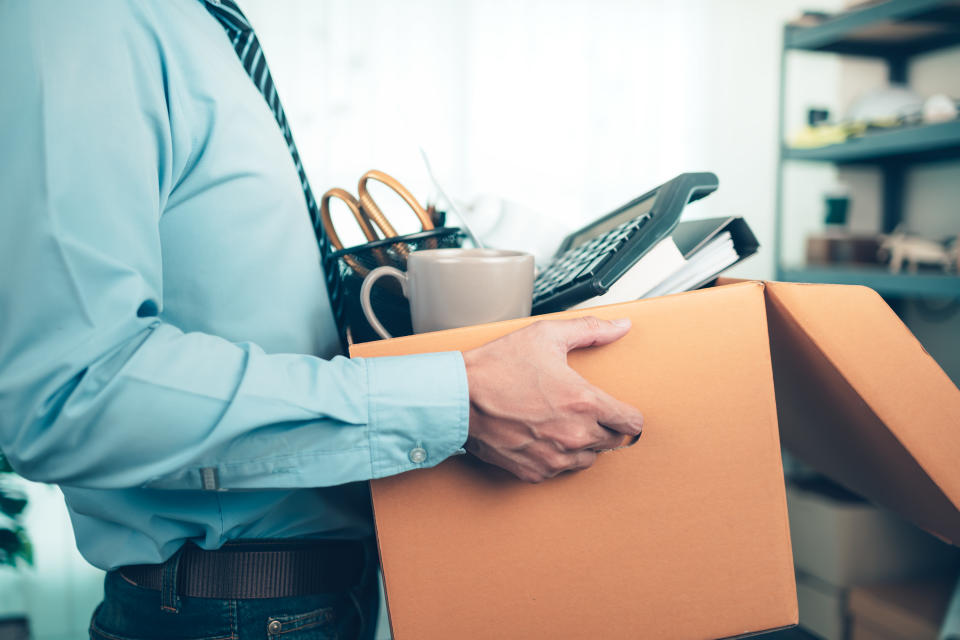 Unemployed man holding cardboard box and resignation letter, dossier, alarm clock, coffee cup, calculator and drawing roll in a box. Resignation from a job, businessman fired or resignation from a job.