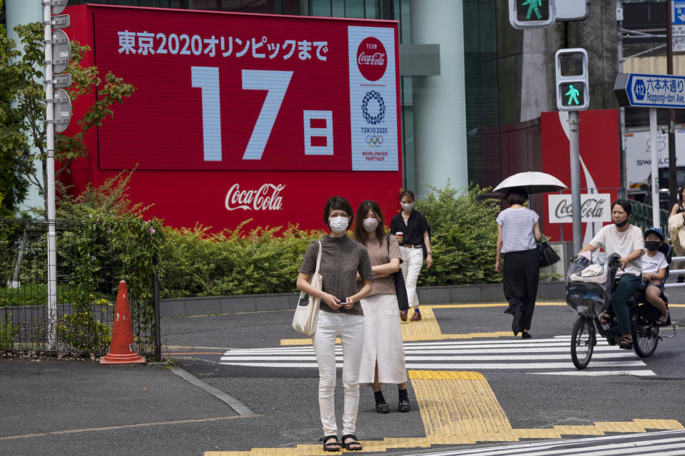 People wearing protective masks wait at a crosswalk as an electric display in the background shows 17 days to Tokyo 2020 Olympics Tuesday, July 6, 2021, in Tokyo. The pressure of hosting an Olympics during a still-active pandemic is beginning to show in Japan. The games begin July 23, with organizers determined they will go on, even with a reduced number of spectators or possibly none at all. (AP Photo/Kiichiro Sato)