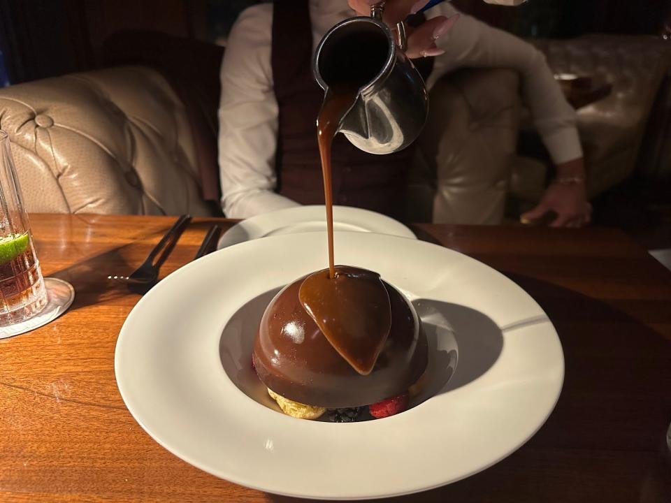 Hot chocolate sauce being poured onto a dessert from a silver kettle.