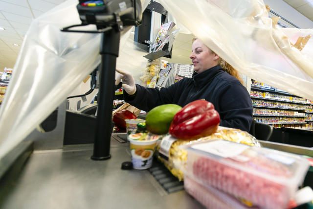 20 March 2020, Schleswig-Holstein, Langballig: Cashier Bianca Krüger scans goods in an Edeka supermarket in the Schleswig-Flensburg district under a plastic foil. With this protective measure, the employees want to protect themselves from possible infection by the customers. Photo: Frank Molter/dpa (Photo by Frank Molter/picture alliance via Getty Images)