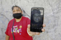 Leticia Valencia Cruz shows a photo of her son Jose Manuel who was disappeared in 2018, near the site where family members who search for disappeared relatives have found 59 bodies, in Salvatierra, Guanajuato state, Mexico, Thursday, Oct. 29, 2020. A Mexican search group said Wednesday it has found 59 bodies in a series of clandestine burial pits in the north-central state of Guanajuato, and that more could still be excavated. (AP Photo/Mario Armas)