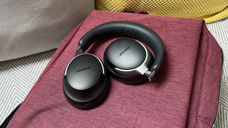 A black pair of Bose QuietComfort Ultra Headphones folded up on a red bag.