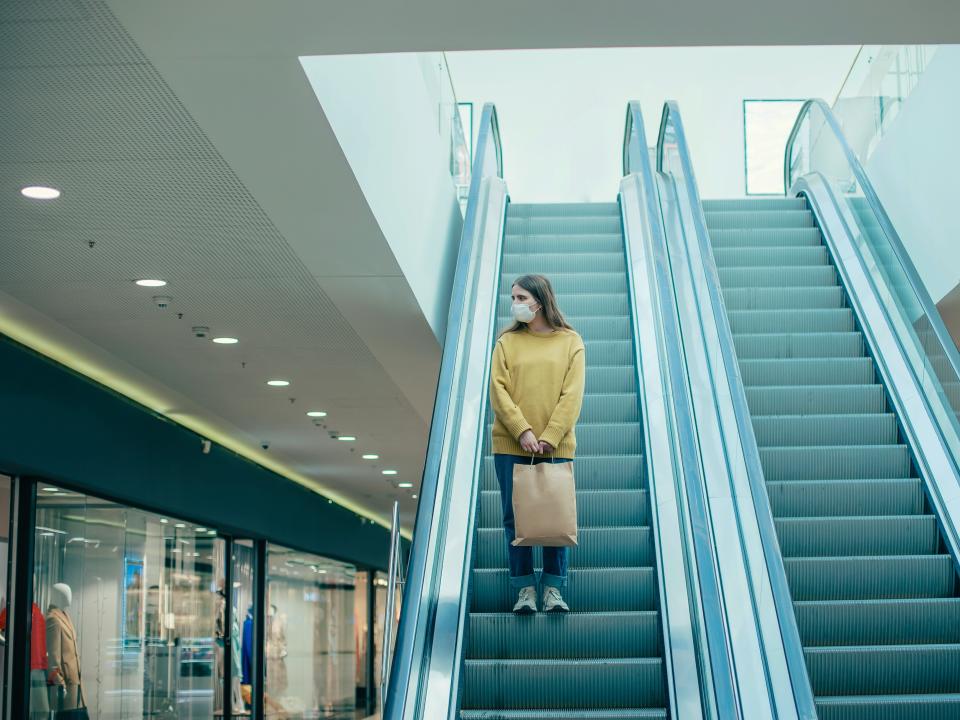 Stock image of a lone woman going down the escalator in an empty shopping mall.