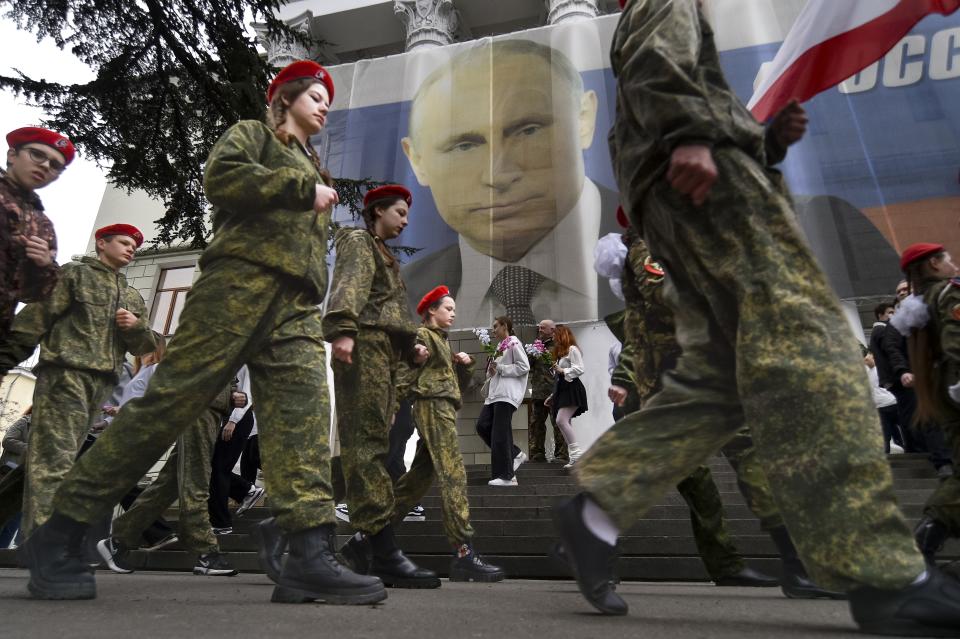 FILE - Youth take part in an action to mark the ninth anniversary of the Crimea annexation from Ukraine with the banner reading: "Russia doesn't start wars, it ends them" next to an image of Russian President Vladimir Putin in Yalta, Crimea, Friday, March 17, 2023. The Crimean Peninsula's balmy beaches have been vacation spots for Russian czars and has hosted history-shaking meetings of world leaders. And it has been the site of ethnic persecutions, forced deportations and political repression. Now, as Russia’s war in Ukraine enters its 18th month, the Black Sea peninsula is again both a playground and a battleground. (AP Photo, File)