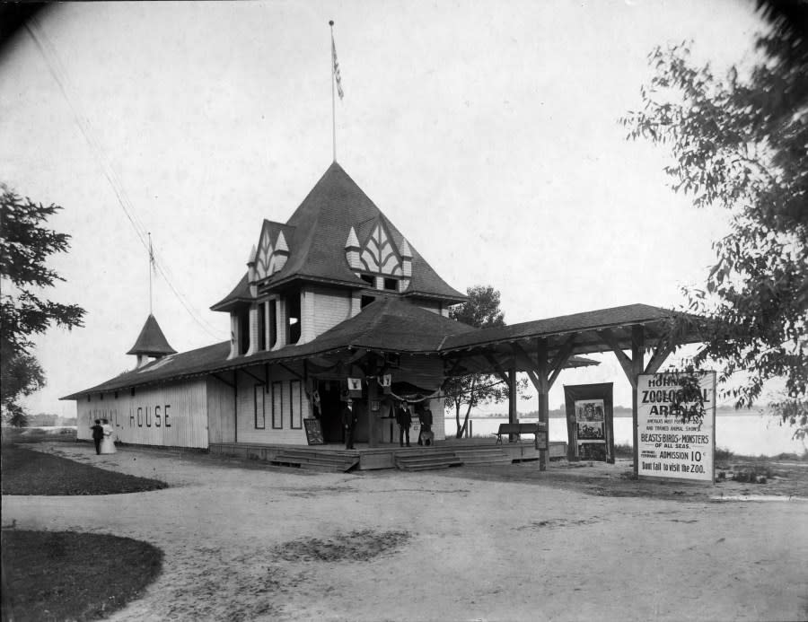 View of an exhibit at Manhattan Beach amusement park in Denver, Colorado; shows people standing on the porch of a building with cupolas and United States flags on poles. Signs read: “Animal House,” “Horn[et?] Zoological Arena, America’s Most Popular Zoo, Beasts Birds, and Monsters of all Seas.” Sloans Lake is in the background. (Denver Public Library Special Collections,X-19523)