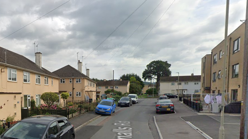 Blue and black cars parked outside peach-coloured homes on residential street. One home has clothes outside drying. 