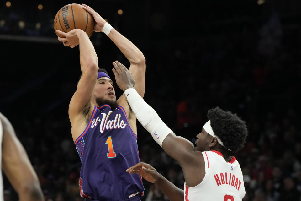 Phoenix Suns guard Devin Booker (1) drives against Houston Rockets guard Aaron Holiday, right, during the first half of an NBA basketball game, Thursday, Feb. 29, 2024, in Phoenix. (AP Photo/Rick Scuteri)