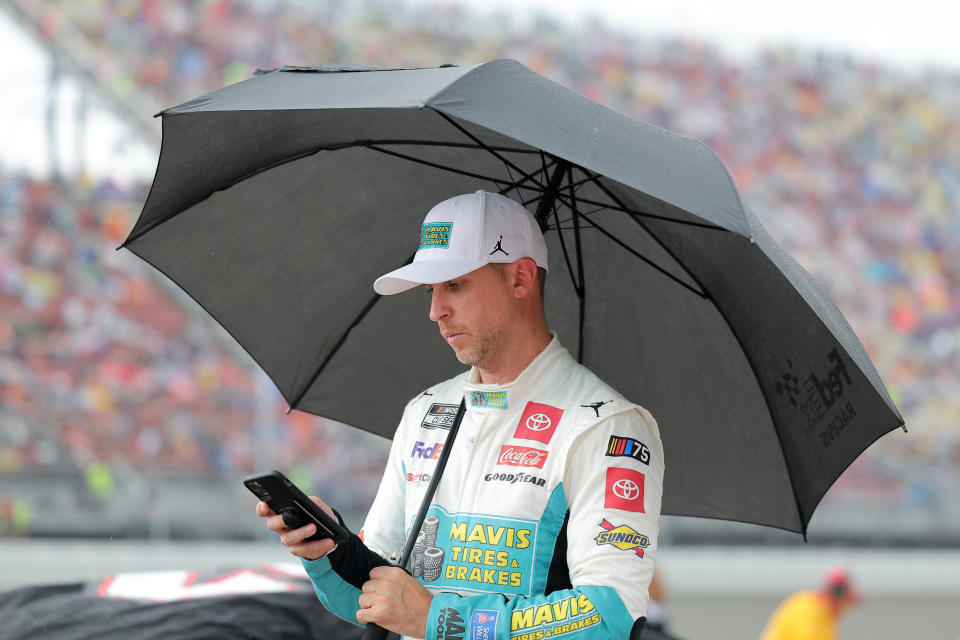 BROOKLYN, MICHIGAN - AUGUST 06: Denny Hamlin, driver of the #11 Mavis Tires & Brakes Toyota, waits on the grid under an umbrella during a weather delay of the NASCAR Cup Series FireKeepers Casino 400 at Michigan International Speedway on August 06, 2023 in Brooklyn, Michigan. (Photo by Jonathan Bachman/Getty Images)