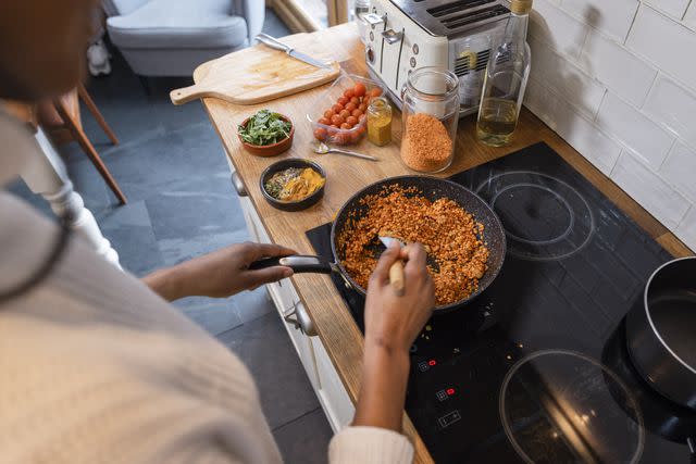 <p>SolStock / Getty Images</p> Young female cooking lentils on the stove with colorful vegetables and spices