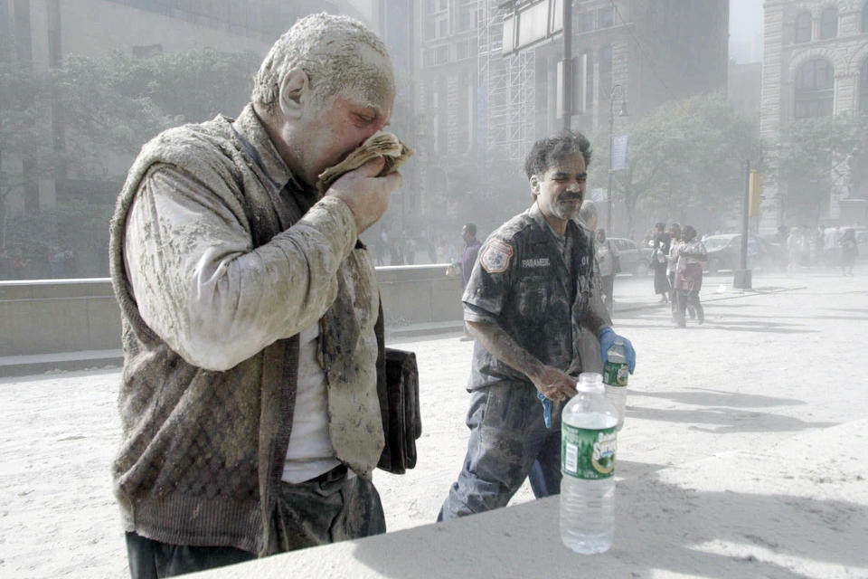 FILE — In this Sept. 11, 2001 file photo, a man coated with dust and debris from the collapse of the World Trade Center south tower coughs near City Hall, in New York. Two decades after the twin towers' collapse, people are still coming forward to report illnesses that might be related to the attacks.(AP Photo/Amy Sancetta, File)