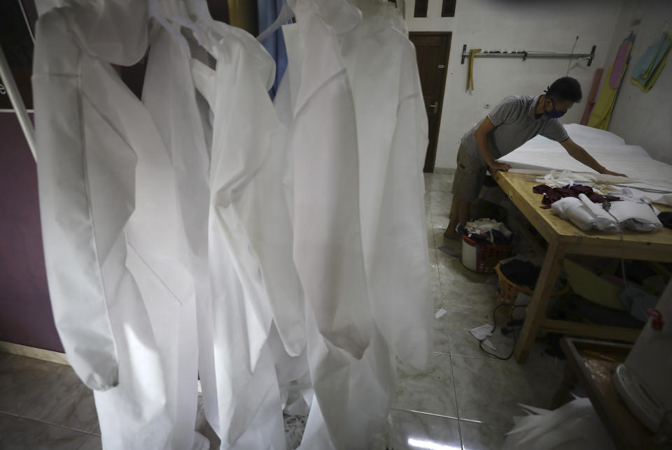 In this Thursday, April 2, 2020 photo, Tating, the owner of a small garment manufacturing business, measures materials as hazmat suits he produces are displayed at his home factory in Depok, Indonesia. When an Indonesian businesswoman Maryati Dimursi heard from friends working in hospitals that they don't have enough proper protective gear when dealing with suspected COVID-19 patients, she decided to help them by crowdfunding to produce proper hazmat suits for distribution to various hospitals in the country. One of her partners, Tating, has three tailors who usually make Muslim clothing for sale online. He’s now postponing other orders to finish the hazmat suits first.(AP Photo/Dita Alangkara)