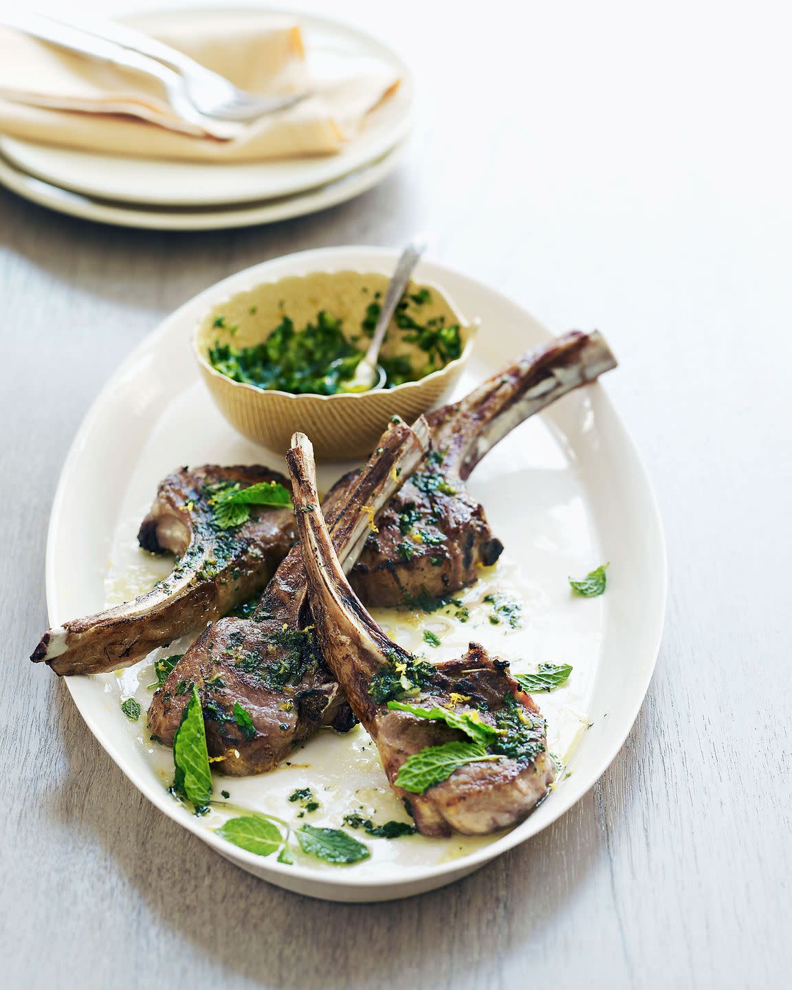 lamb chops with mint gremolata on a white oval serving plate with a small bowl of the gremolata