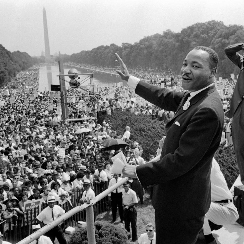 Martin Luther King Jr. delivers a speech at the March on Washington, waving to a large crowd near the Lincoln Memorial with the Washington Monument in the background