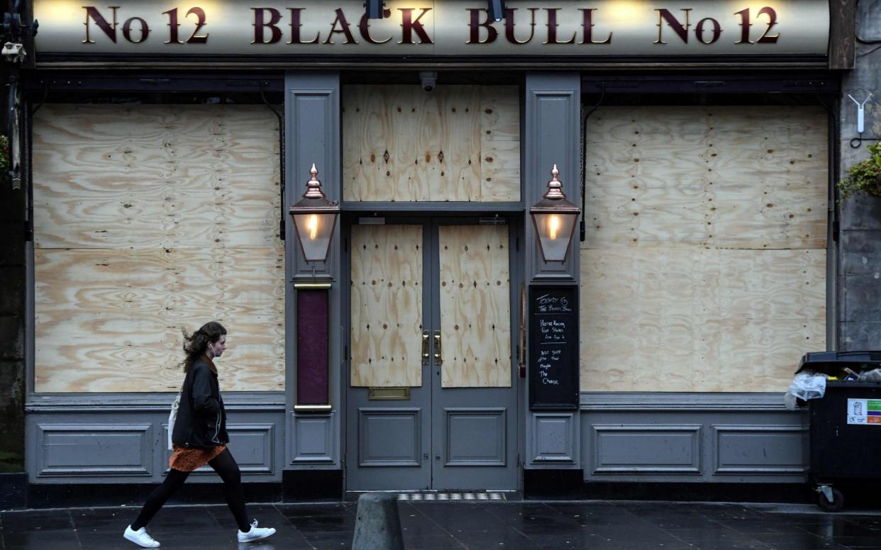 A woman walks past a closed pub in The Grassmarket, Edinburgh last year - AFP