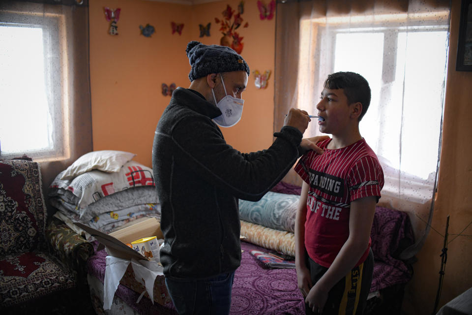 Valeriu Nicolae shows a boy how to correctly brush his teeth in Nucsoara, Romania, Saturday, Jan. 9, 2021. A gentle hero to many in Romania, Valeriu Nicolae says that, at heart, he is more like former NBA star Michael Jordan — highly competitive and eager to improve in what he does best. In Nicolae’s case that is helping others. The rights activist has earned praise for his tireless campaign to change for the better the lives of the Balkan country’s poorest and underprivileged residents, particularly the children. (AP Photo/Andreea Alexandru)